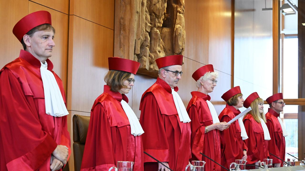 Die Richterinnen und Richter stehen nebeneinander. Sie haben rote Kleidung an. Das ist typisch für die Richter an diesem Gericht. Eine Richterin hält ein Papier in der Hand. Sie liest etwas vor. 