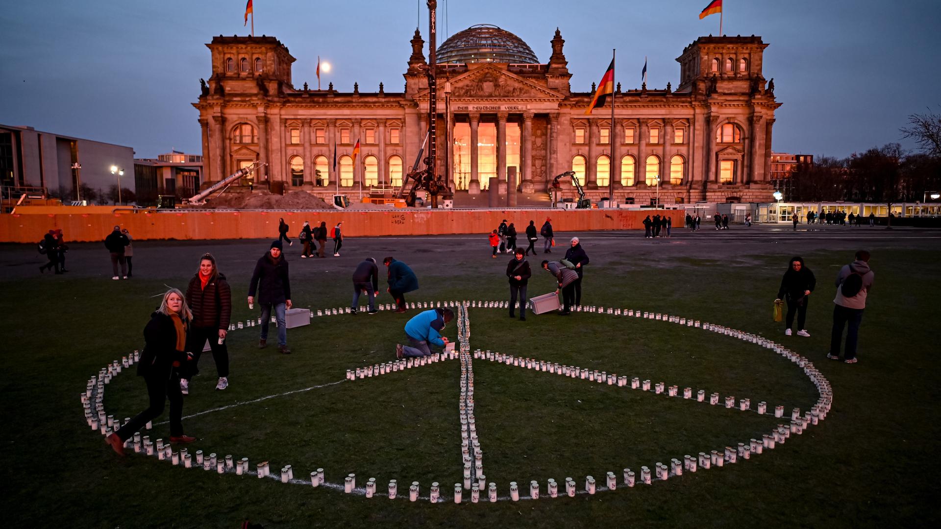 Vor dem Reichtagsgebäude haben Menschen Kerzen abgelegt. Sie bilden das Friedenssymbol.