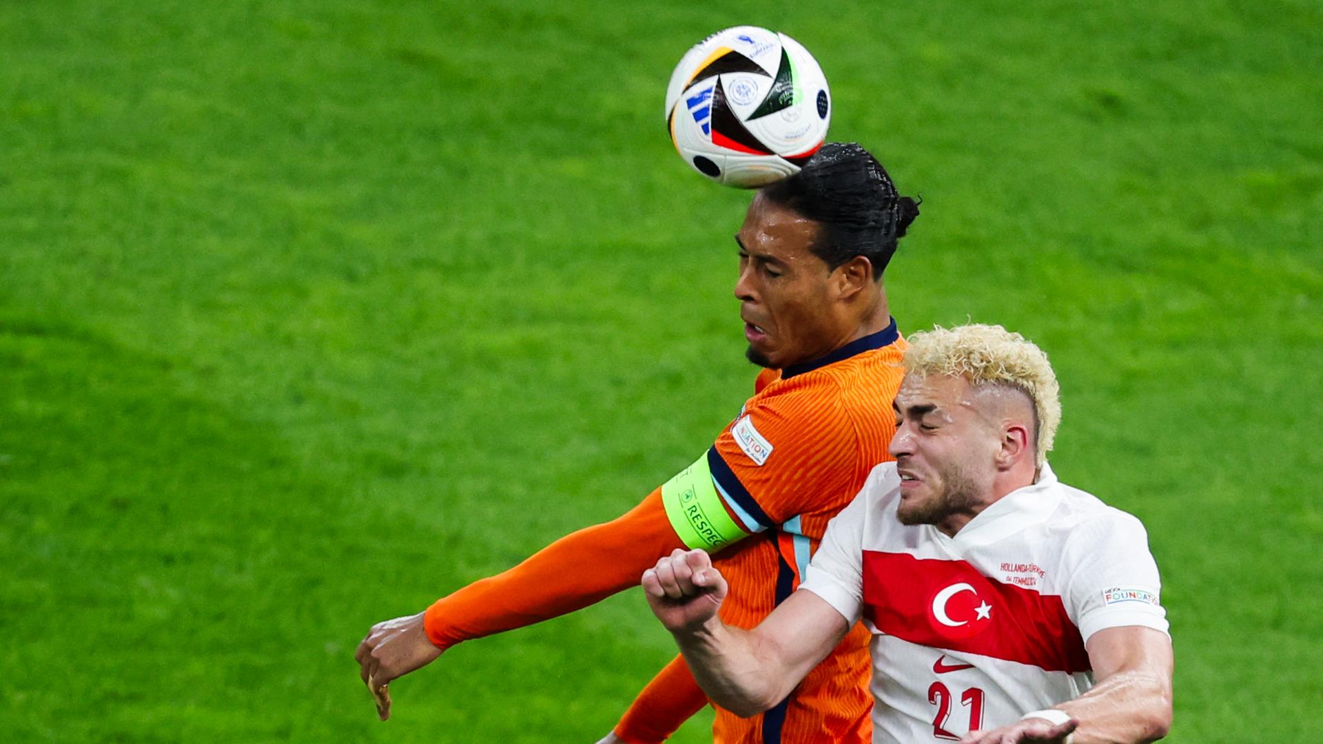 Ein niederländischer und ein türkischer Spieler springen mit zusammengekniffenen Augen in die Luft, um den Ball zu köpfen. 