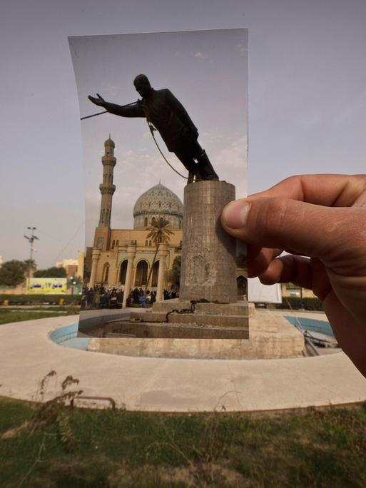 Eine Hand hält ein Foto an dem Platz, wo das Denkmal von Saddam Hussein 2003 gestürzt wurde.