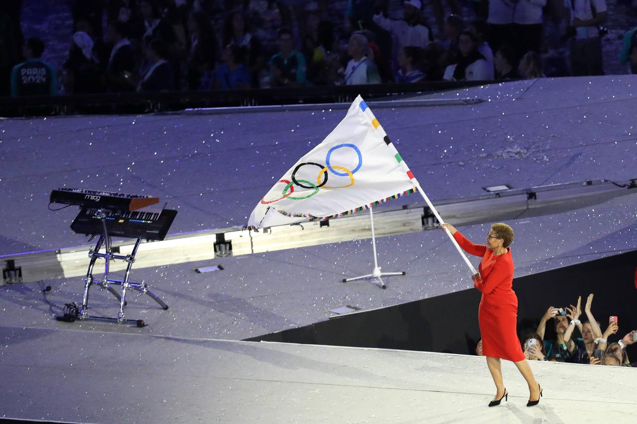 Zu sehen ist, wie die Bürgermeisterin von Los Angeles in einem roten Kleid auf der Bühne die Olympische Flagge schwenkt.