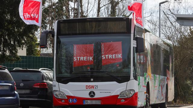 Ein leerer Bus steht auf einem Parkplatz. Hinter den Scheiben hängen Schilder mit der Aufschrift "Streik".