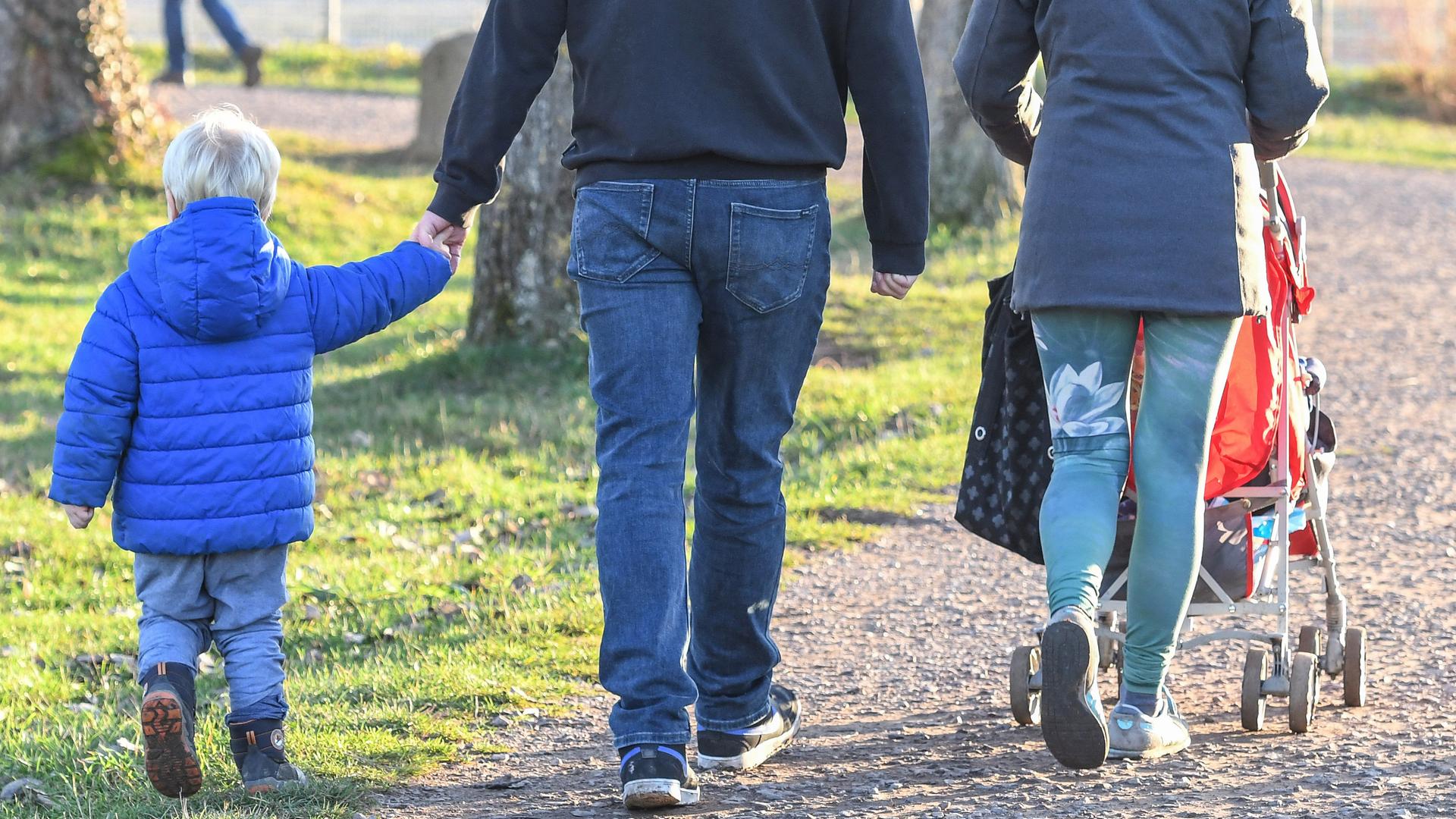 Eine Vater und eine Mutter gehen mit einem Kleinkind und einem Kinderwagen spazieren. Eine Vater und eine Mutter gehen mit einem Kleinkind und einem Kinderwagen spazieren.