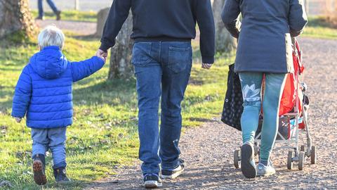 Eine Vater und eine Mutter gehen mit einem Kleinkind und einem Kinderwagen spazieren. 