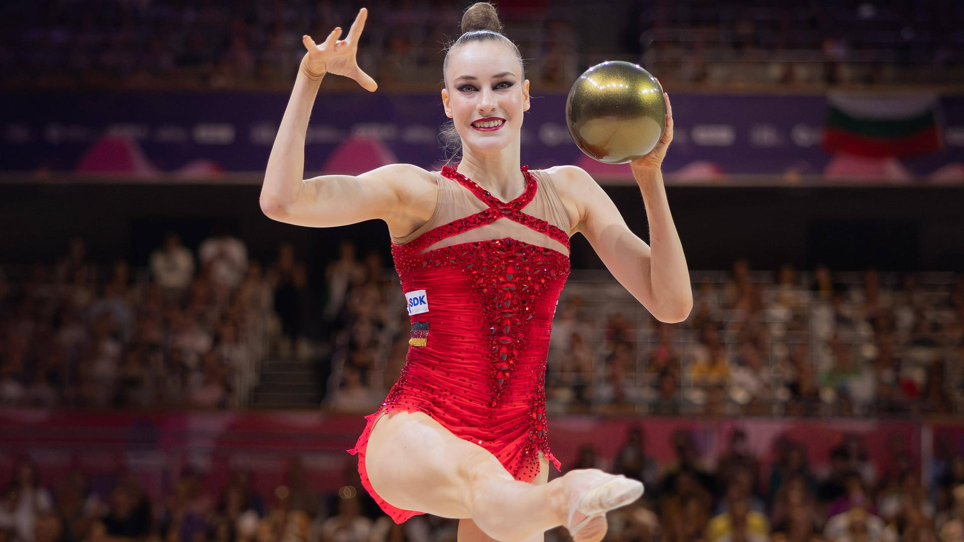 Darja Varfolomeev tanzt, während sie einen großen glänzenden Ball in der linken Hand hält.