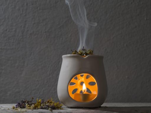 Kräuter werden in einer Duftlampe über einem Teelicht verbrannt. Der Rauch steigt nach oben.
