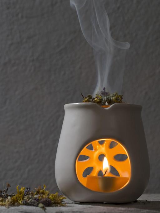Kräuter werden in einer Duftlampe über einem Teelicht verbrannt. Der Rauch steigt nach oben.
