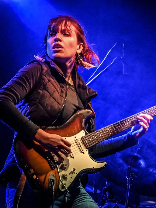 Monika Roscher steht auf der Bühne und spielt in blaues Licht getaucht Gitarre