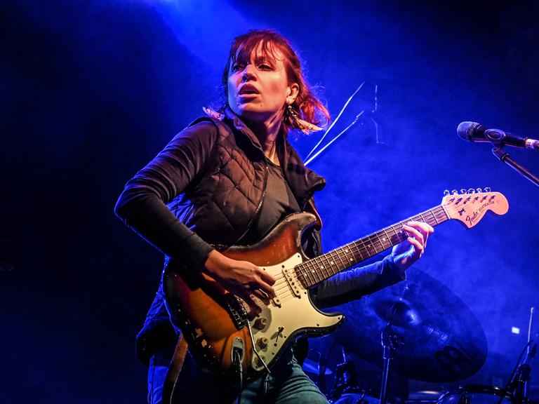 Monika Roscher steht auf der Bühne und spielt in blaues Licht getaucht Gitarre