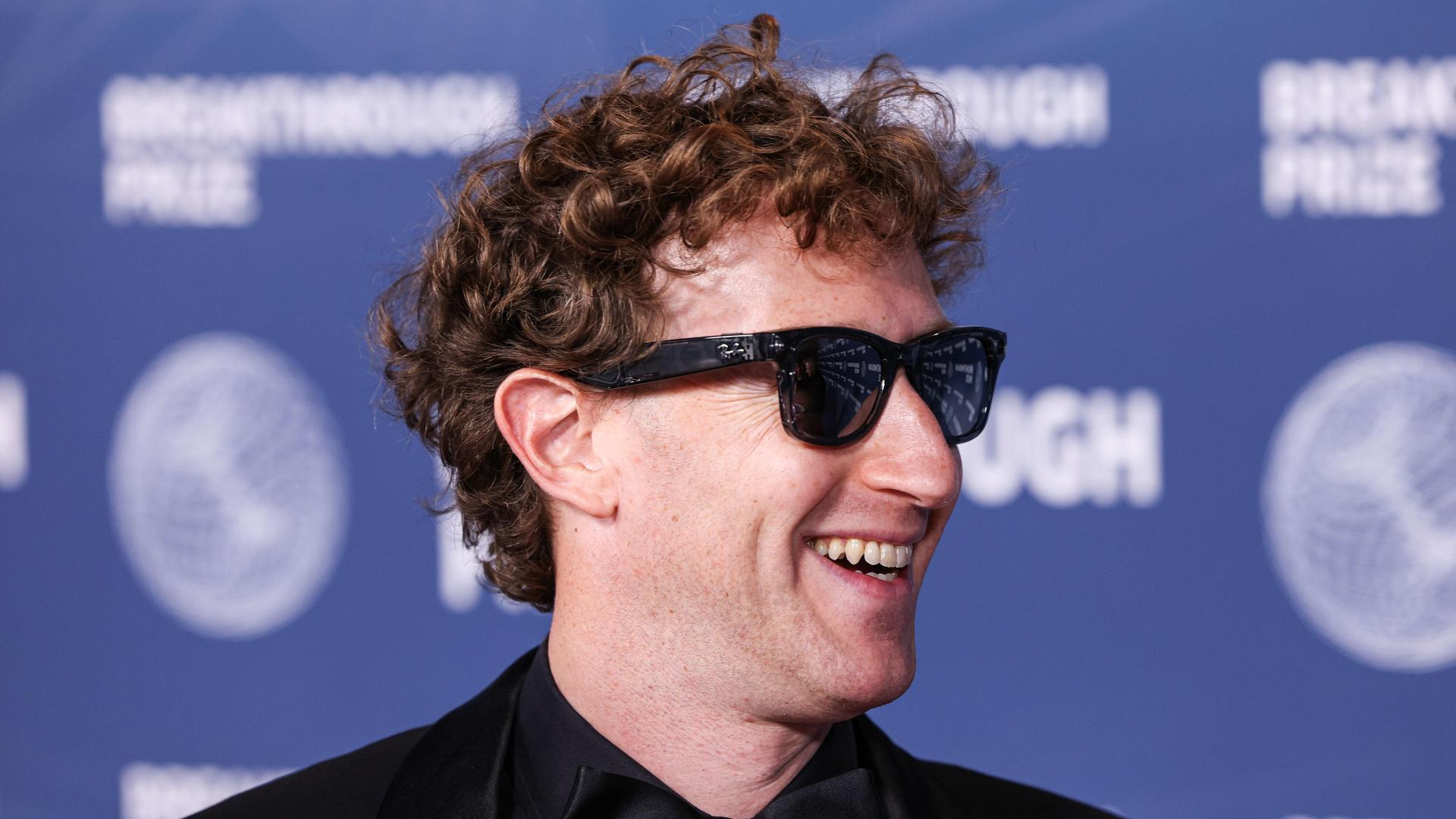 Der Meta-CEO Mark Zuckerberg trägt eine dunkel getönte Sonnenbrille, lächelt und schaut nach rechts.