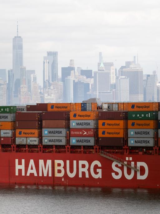 Ein Containerschiff liegt im New Yorker Hafen vor Anker. Es trägt die Aufschrift "Hamburg Süd". Im Hintergrund ist die Skyline von New York zu sehen.