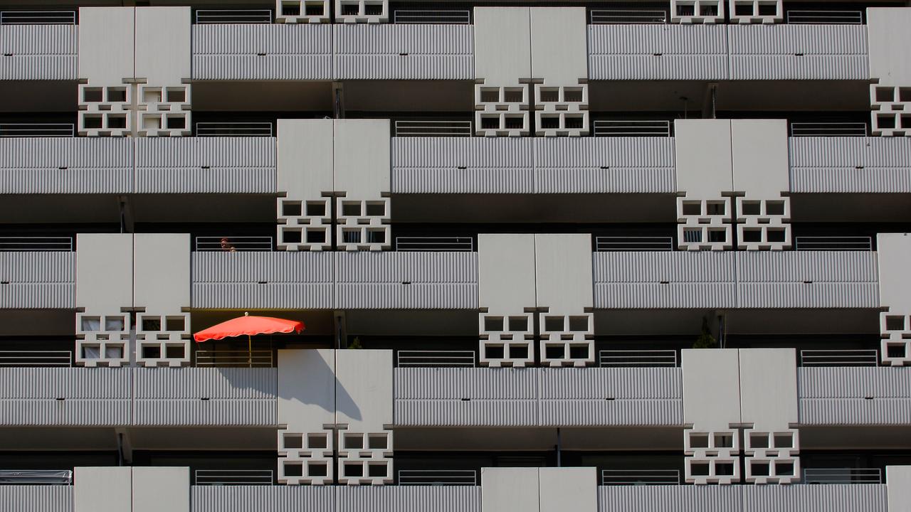 Blick auf eine grauen Häuser-Fassade mit mehreren Balkons - auf einem davon ist ein roter Sonnenschirm zu sehen.