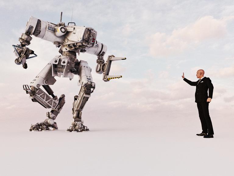 Ein Mann mit Anzug hält eine Hand hoch, um einen rieseigen Roboter zu stoppen.