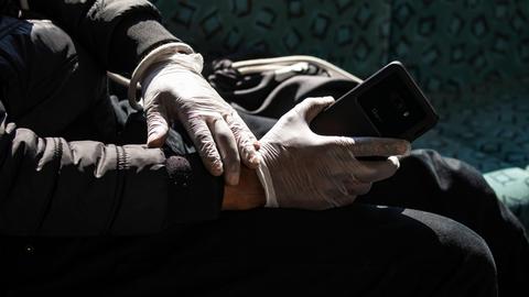 Eine Person in schwarzer Jacke hält sein Smartphone mit Schutzhandschuhen in der S-Bahn am Alexanderplatz in Berlin.