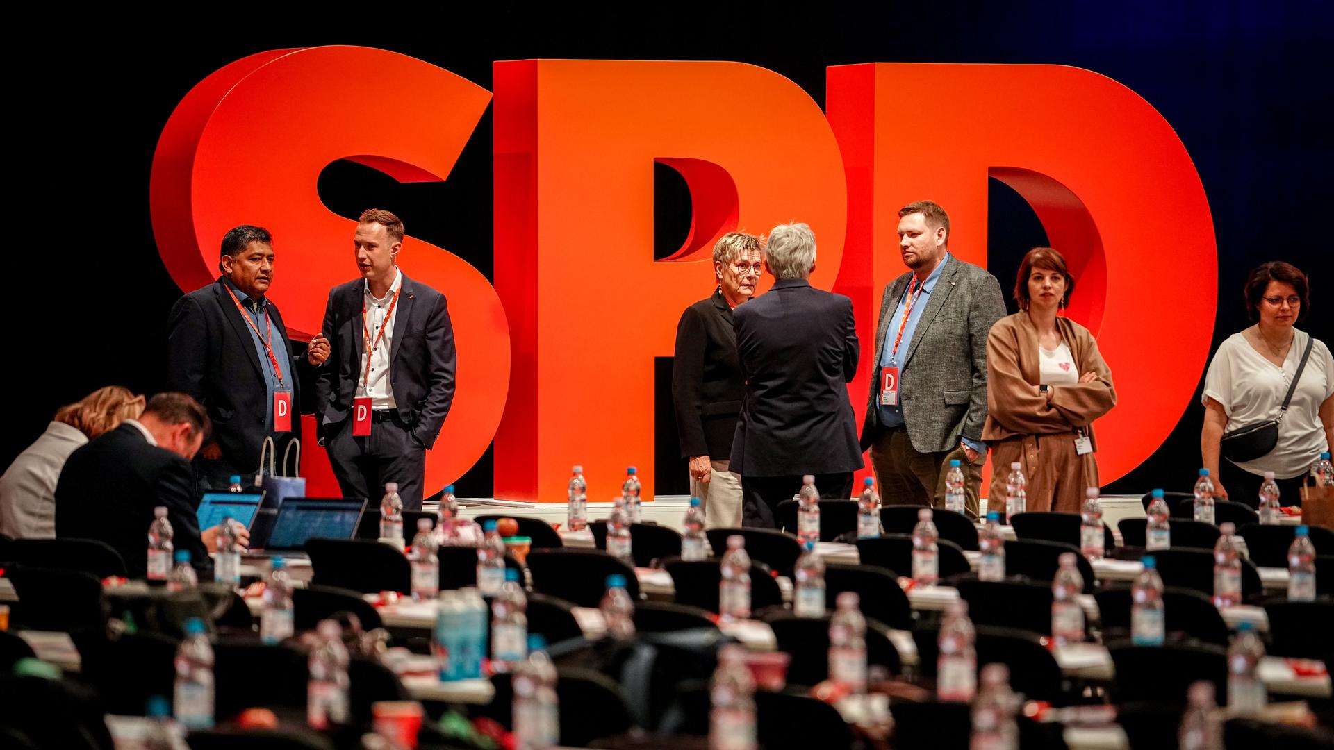 Auf der Bühne vor einem SPD-Schriftzug aus stehenden großen roten Buchstaben stehen mehrere Teilnehmer und reden. Im Vordergrund unscharf die Delegiertenbänke. Auf der Bühne vor einem SPD-Schriftzug aus stehenden großen roten Buchstaben stehen mehrere Teilnehmer und reden. Im Vordergrund unscharf die Delegiertenbänke.