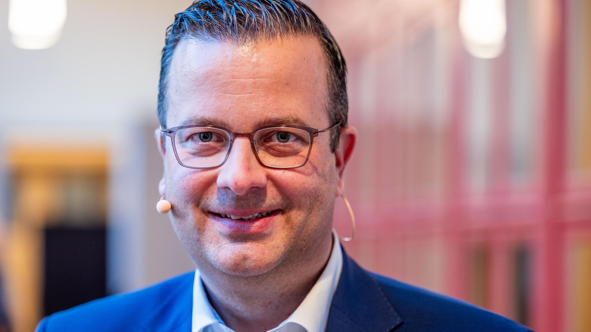 Ehlers blickt in die Kamera und lächelt. Er trägt eine Brille und ein Headset.