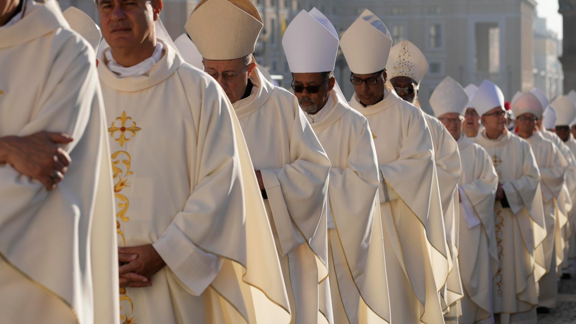 Zu sehen sind katholische Bischöfe im weißen Ornat auf dem Weg zur Synode in Rom.