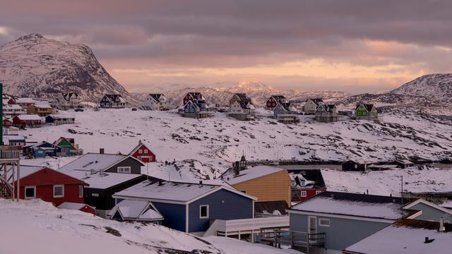 Verschneite Häuser in der grönländischen Hauptstadt Nuuk, hinter Wolken leuchtet die tiefstehende Sonne.