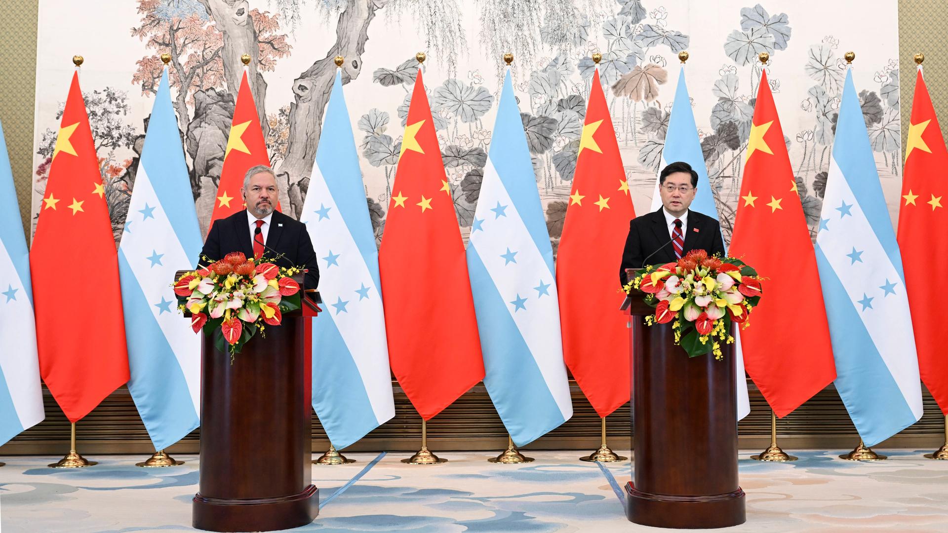 Das Foto zeigt Chinas Außenminister Qin Gang und den honduranischen Außenminister Eduardo Reina in Peking. Sie stehen hinter mit Blumen geschmückten Rednerpulten, im Hintergrund sind mehrere Flaggen der beiden Staaten drappiert. Das Foto zeigt Chinas Außenminister Qin Gang und den honduranischen Außenminister Eduardo Reina in Peking. Sie stehen hinter mit Blumen geschmückten Rednerpulten, im Hintergrund sind mehrere Flaggen der beiden Staaten drappiert.