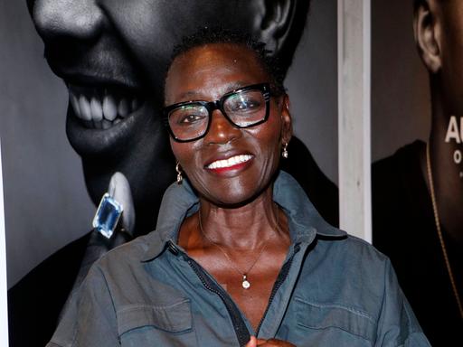 Auma Obama lacht in die Kamera. Sie trägt eine blaue Bluse und eine schwarz umrandete Brille.