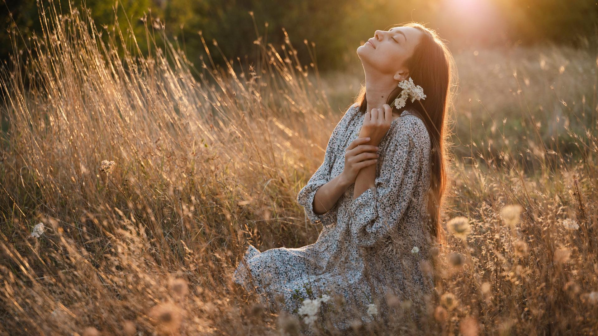 Carefree woman with flower sitting in meadow at sunset model released, Symbolfoto, ALKF01118