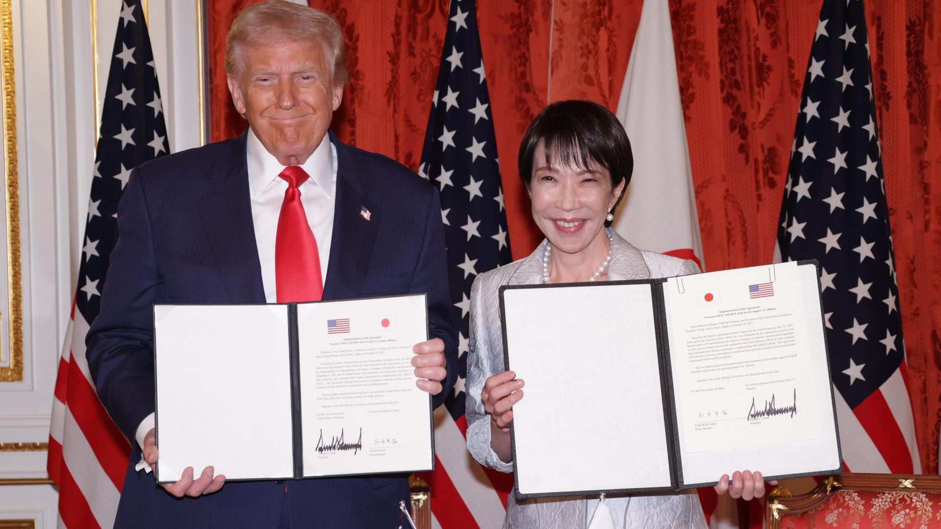 US-Präsident Trump und Japans Premierministerin Takaichi halten beide ein unterzeichnetes Abkommen in den Händen und lächeln in die Kamera. US-Präsident Trump und Japans Premierministerin Takaichi halten beide ein unterzeichnetes Abkommen in den Händen und lächeln in die Kamera.