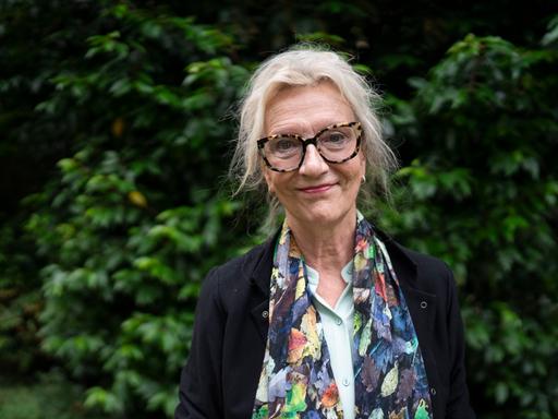 Elizabeth Strout trägt Brille, ein schwarzes Sakko und einem farbig gemusterten Schal und schaut freundlich in die Kamera.
