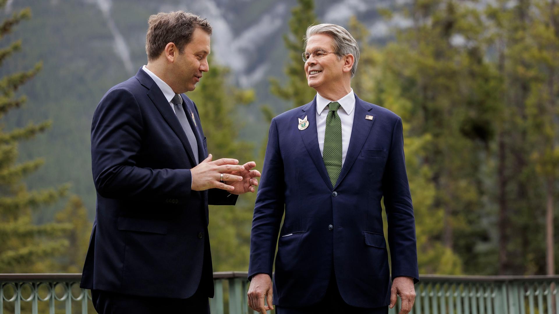 Bundesfinanzminister Lars Klingbeil (SPD) und sein US-Kollege Scott Bessent stehen in Anzug und Krawatte vor der Bergkullise der kanadischen Rocky Mountains und reden.