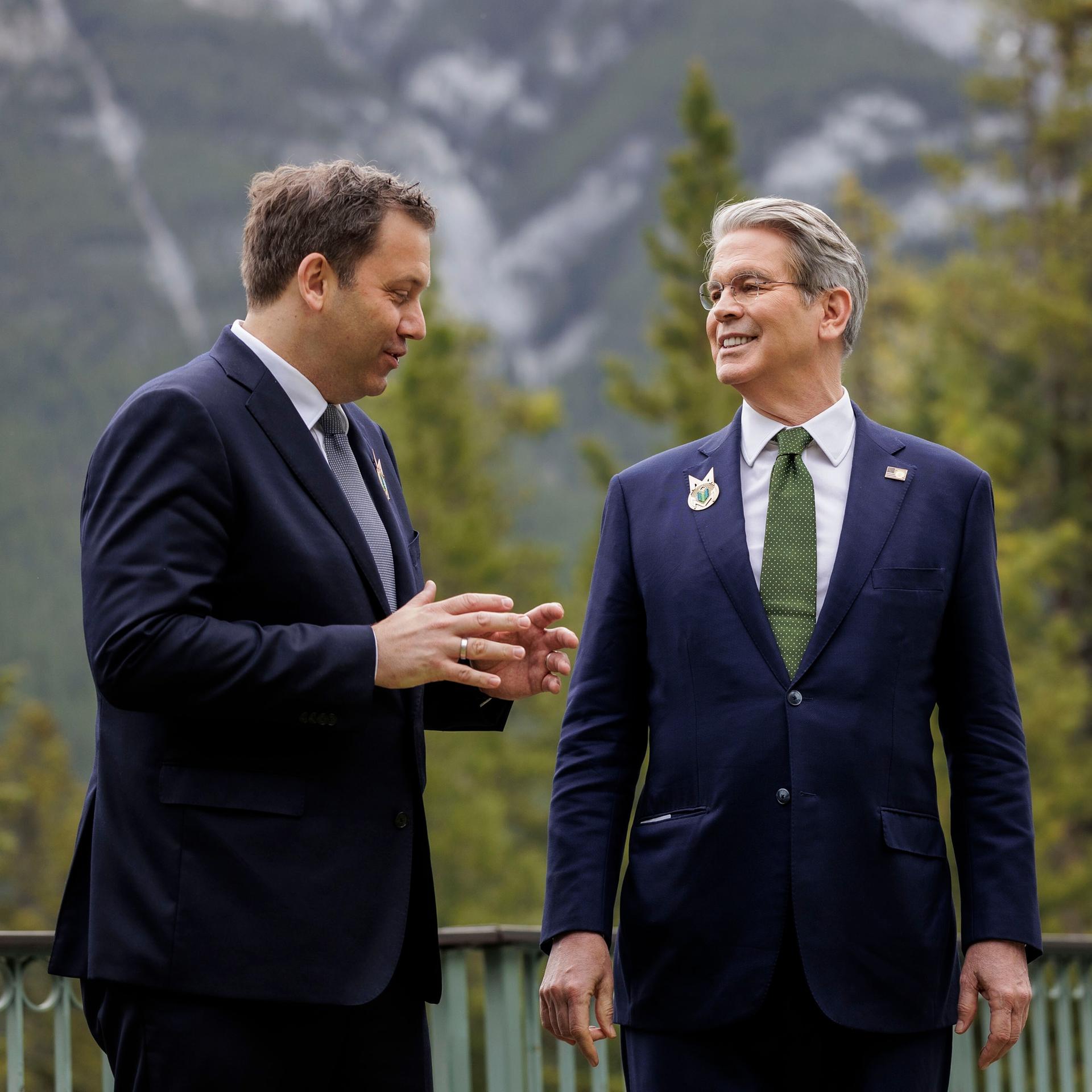 Bundesfinanzminister Lars Klingbeil (SPD) und sein US-Kollege Scott Bessent stehen in Anzug und Krawatte vor der Bergkullise der kanadischen Rocky Mountains und reden.