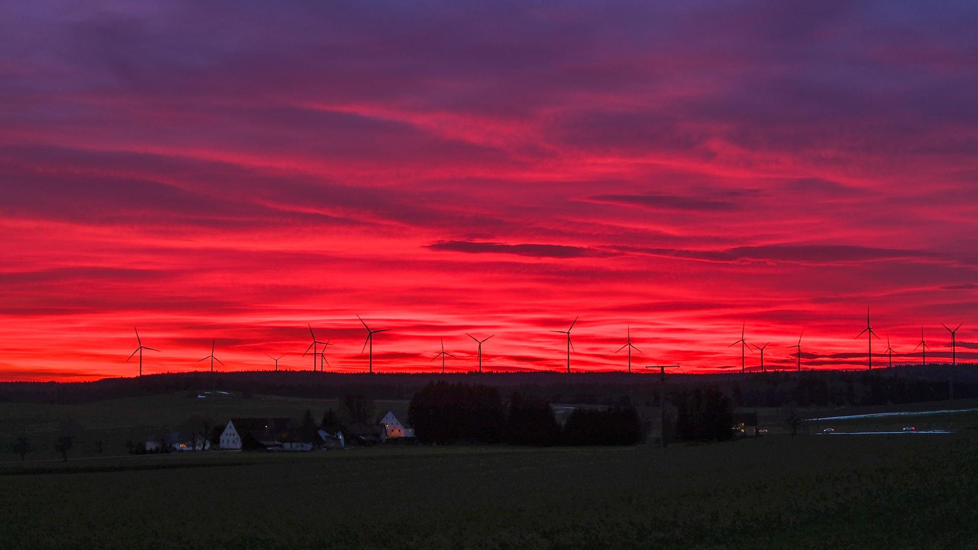 Auf der Schwäbischen Alb geht am Abend die Sonne unter. Hinter den Windrädern leuchtet das Abendrot.