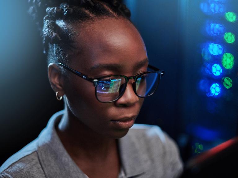 Junge afrikanische Frau, die in einem Serverraum auf einen Computerbildschirm schaut (Symbolbild)