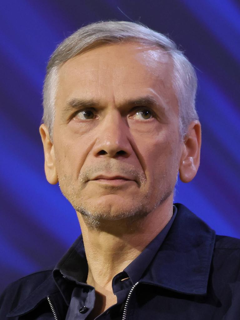 Lutz Seiler sitzt auf einer Bühne mit blauem Hintergrund und schaut leicht zur Seite.