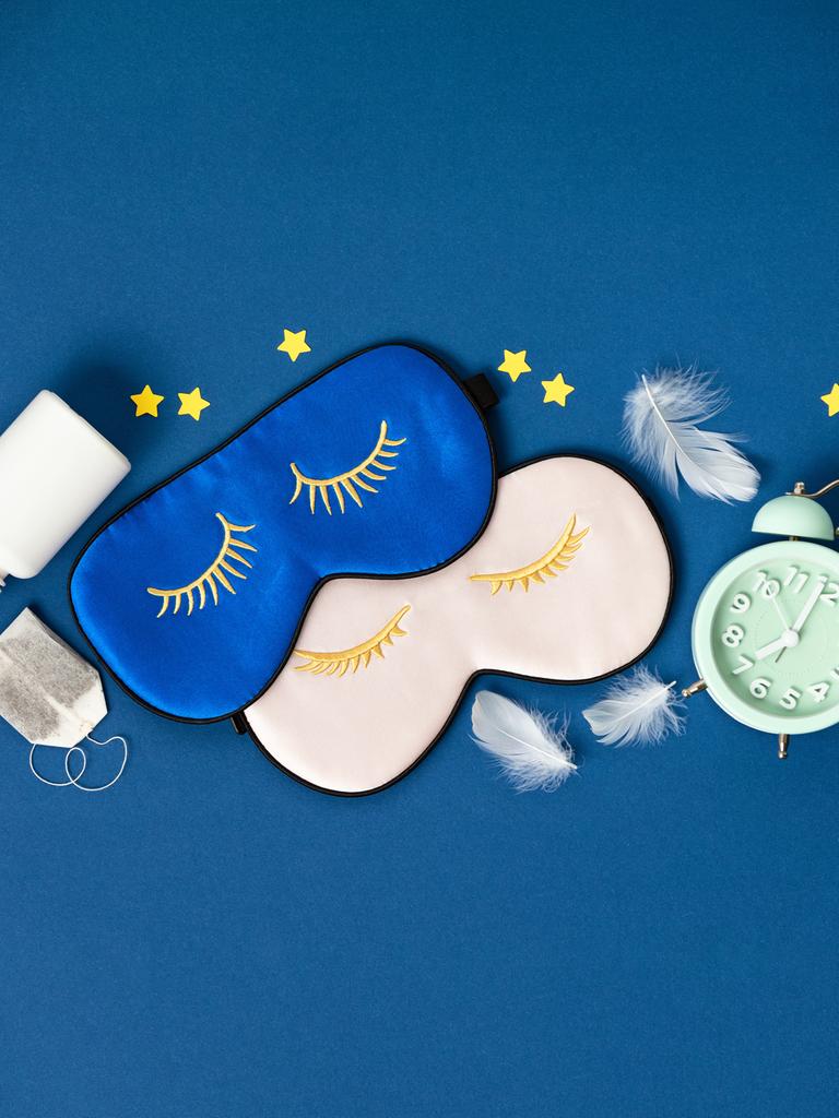 Blaue und rosa Schlafmasken, Tabletten und Kräutertee liegen auf blauem Hintergrund.