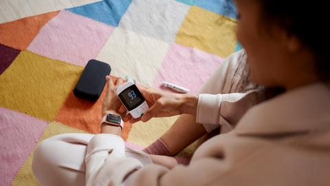 Eine junge Frau überprüft ihren Blutzucker mit einem Messgerät und versucht, ihn mit einer Smartwatch-App zu synchronisieren.