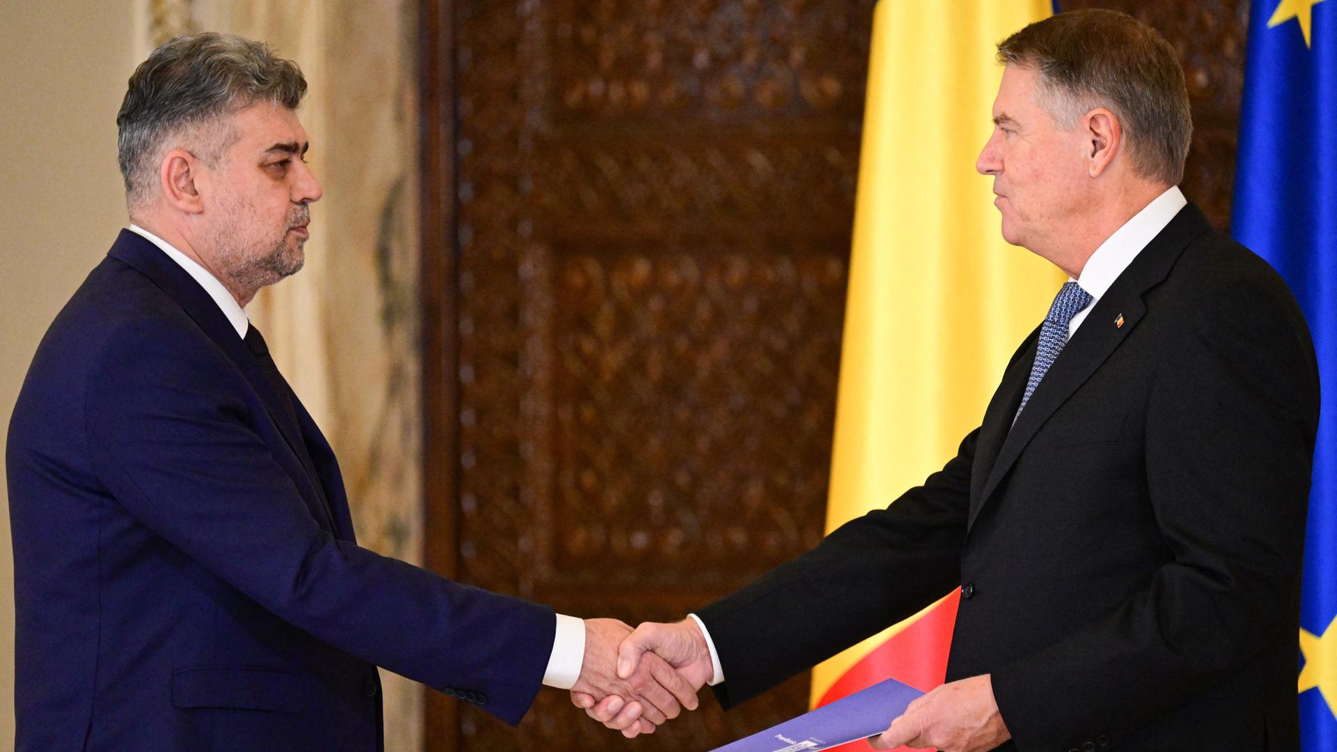 Marcel Ciolacu (l) und Klaus Iohannis während der Vereidigungszeremonie im Cotroceni Palast in Bukarest. Iohannis schüttelt Cioalacu die Hand und hält in der anderen eine Urkunde.