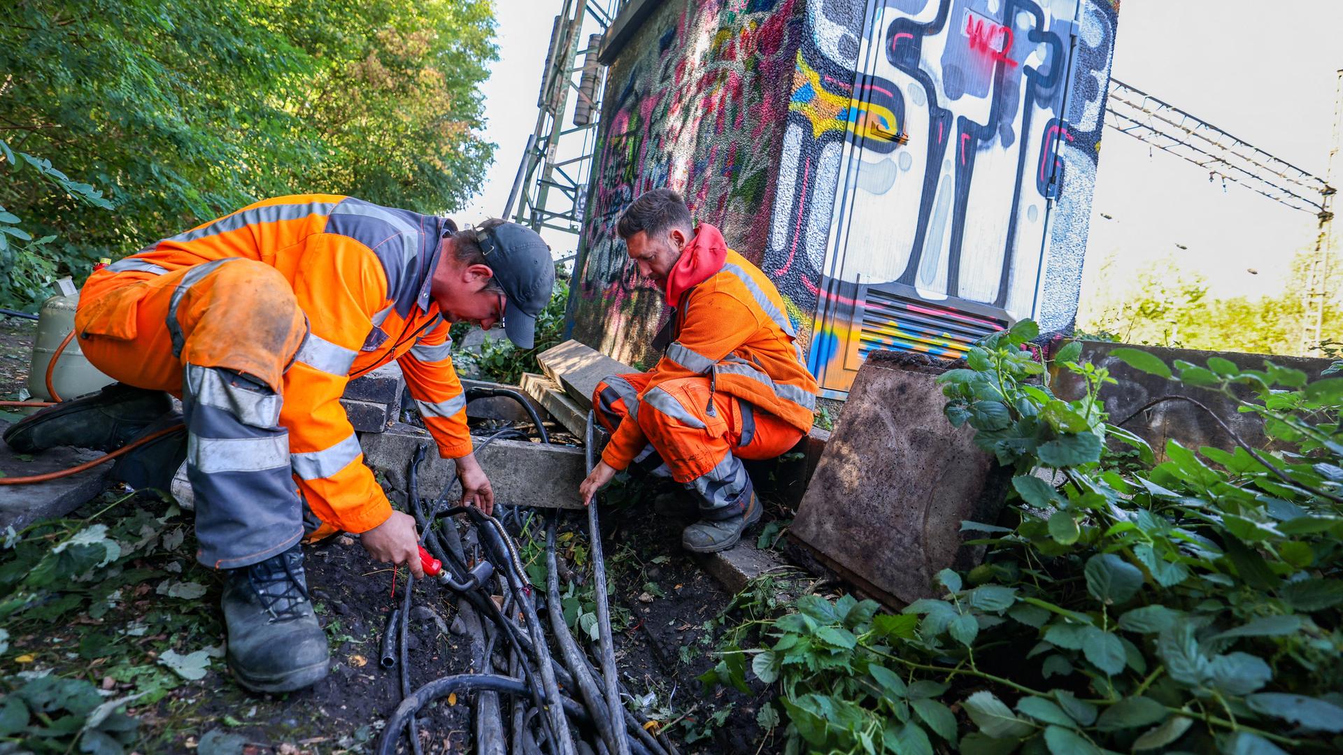Zwei Mitarbeiter in orangefarbenen Schutzanzügen arbeiten an Bahngleisen.