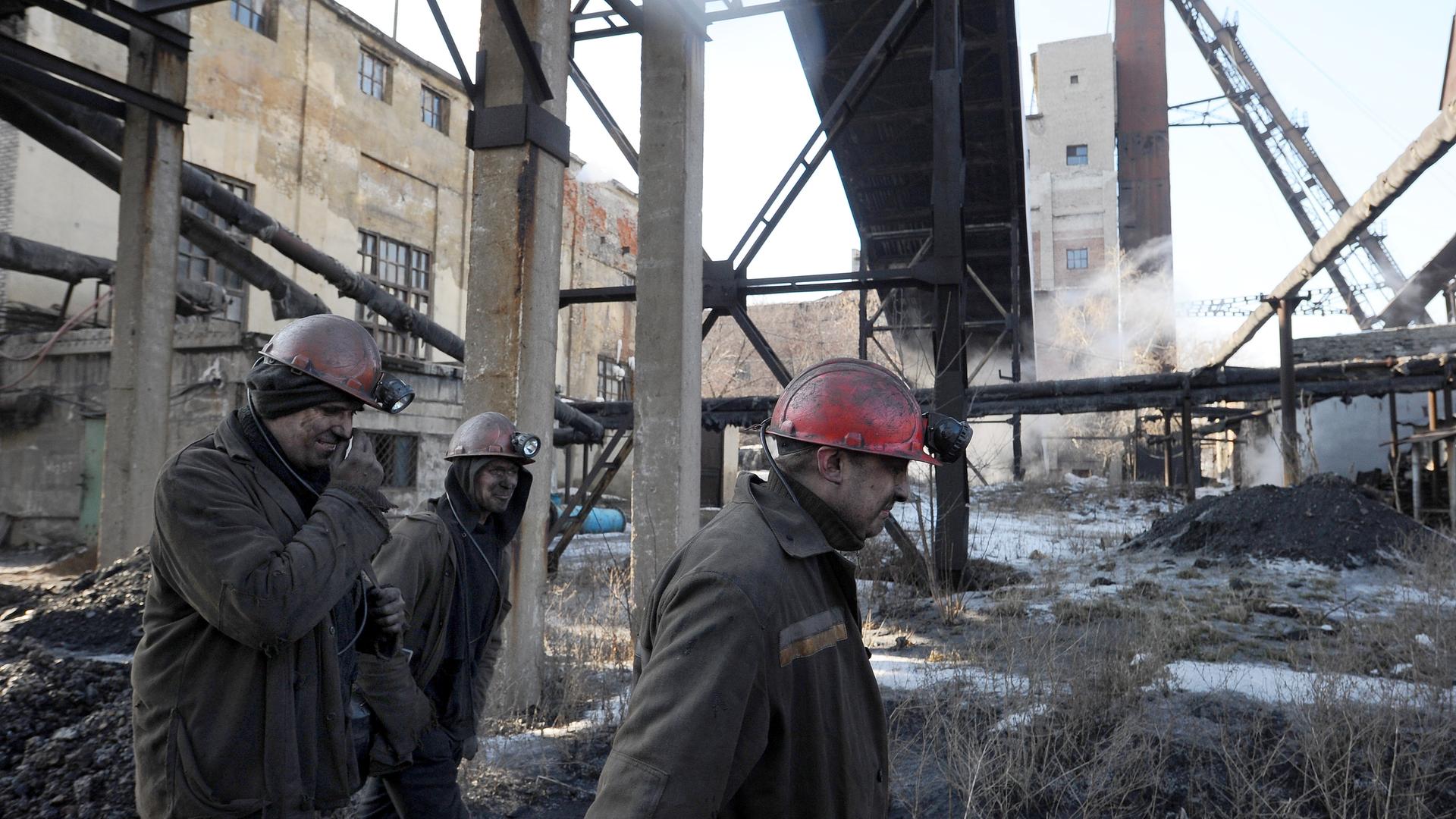 Bergarbeiter gehen über das Gelände einer Kohlemine mit vielen Gebäuden, Strahlkonstruktionen und anderen Bauten.