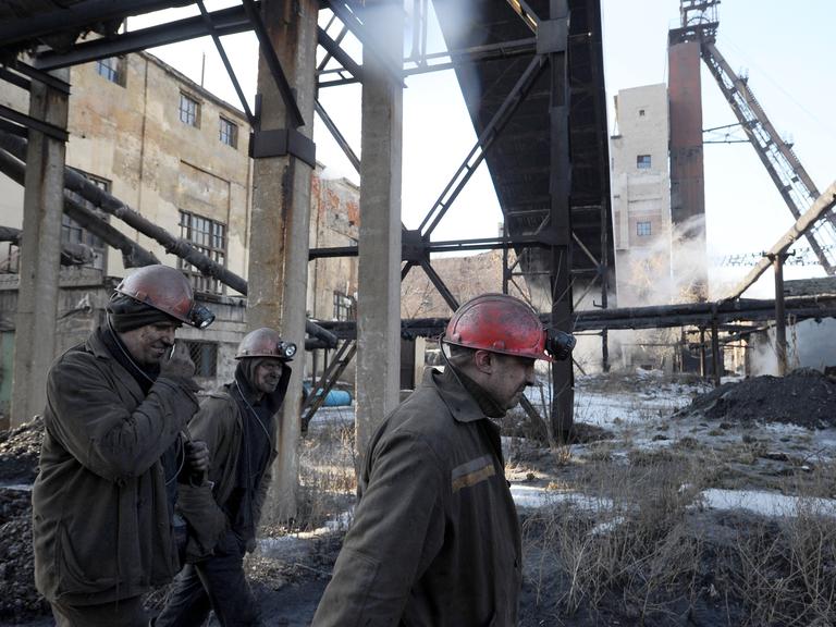 Bergarbeiter gehen über das Gelände einer Kohlemine mit vielen Gebäuden, Strahlkonstruktionen und anderen Bauten.