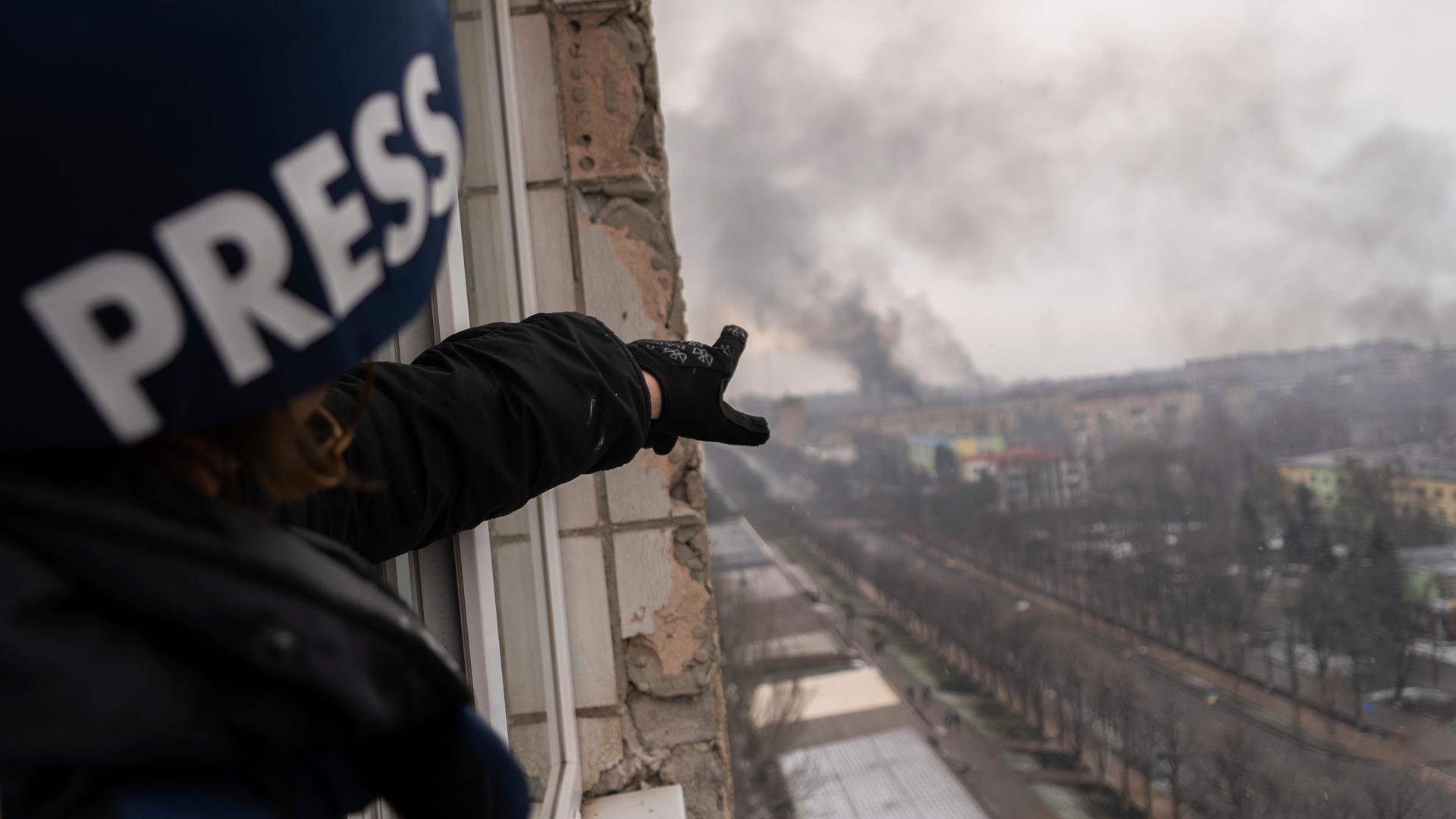 Das englische Wort "Press" für Presse steht auf dem Helm einer Fotografin, die auf Rauch über der ukrainischen Stadt Mariupol zeigt. 