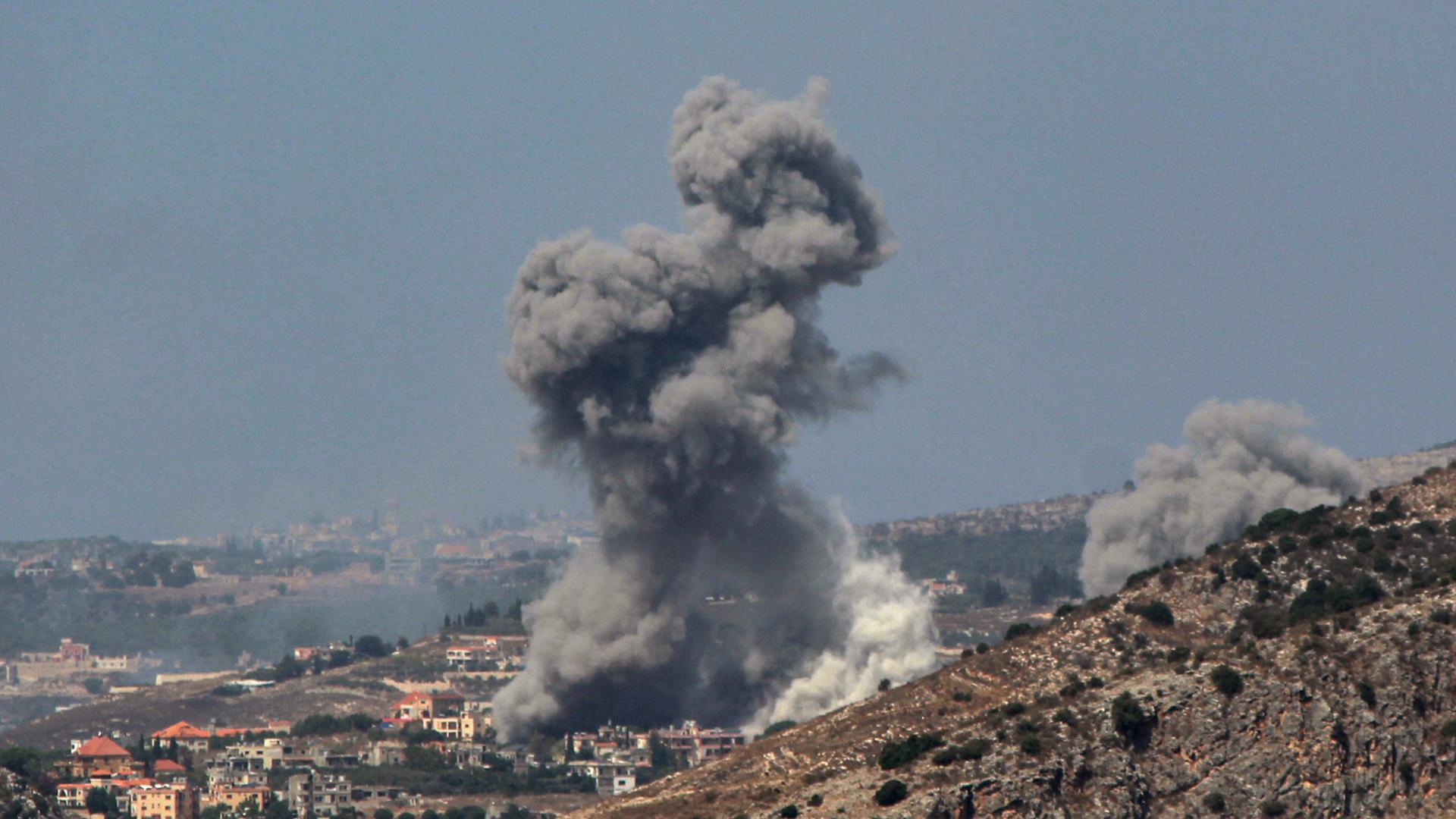Rauch steigt aus einem Dorf in den Bergen auf.