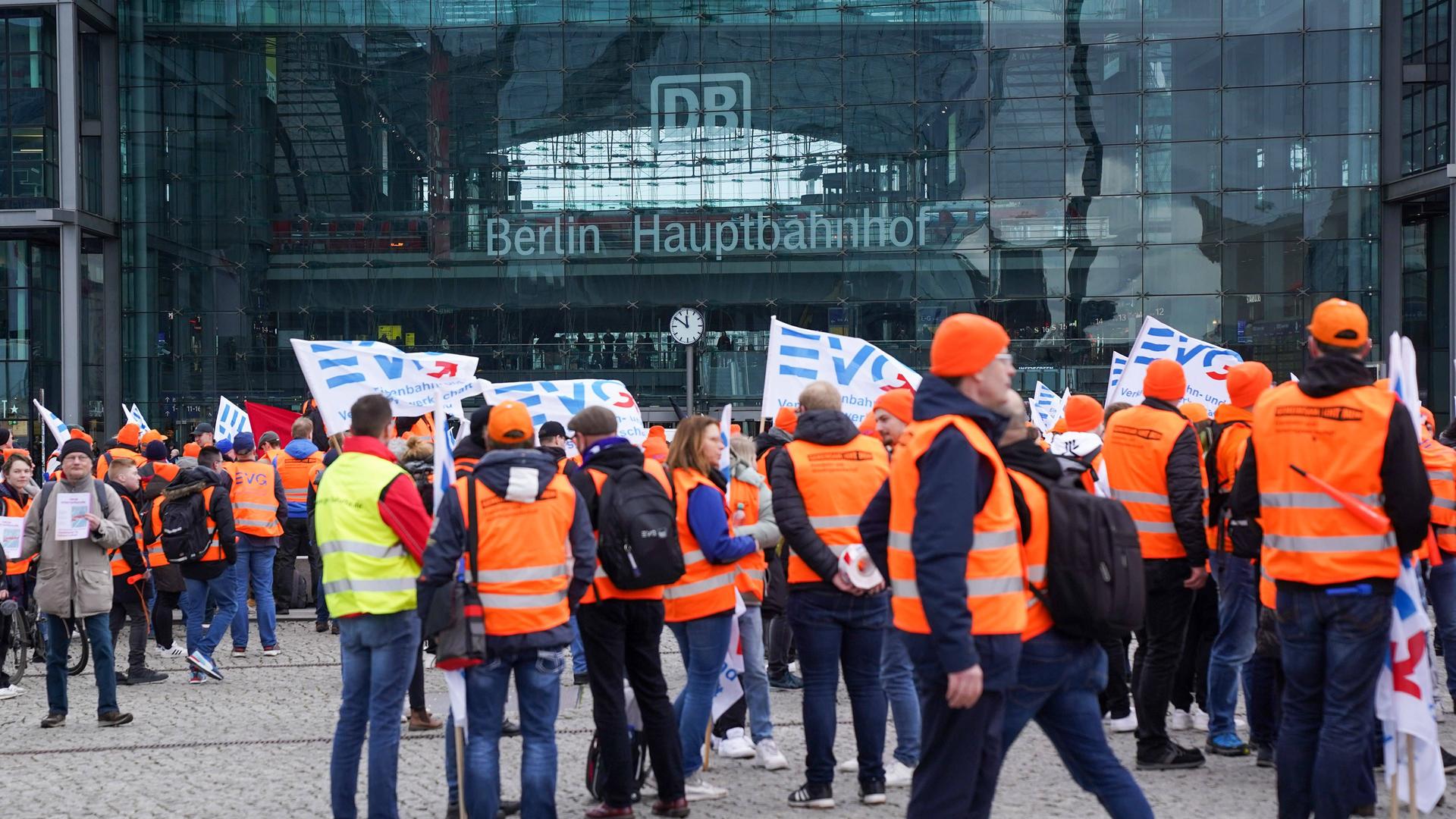 Berlin, Deutschland: Demonstration der EVG vor dem Berliner Hauptbahnhof. Mehrere Personen haben orangene Westen an und einige halten EVG-Fahnen in der Hand.