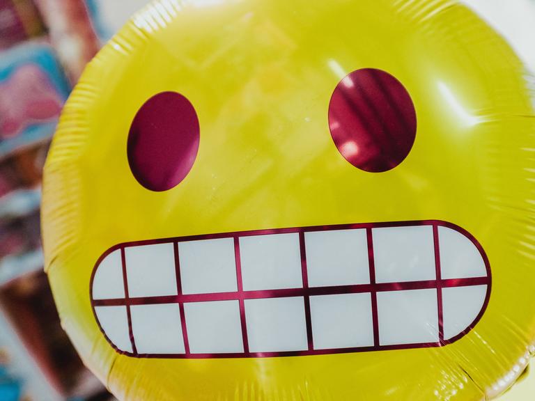 Ein runder gelber Ballon mit einem Emoji-Gesicht, das Zähne zeigt.