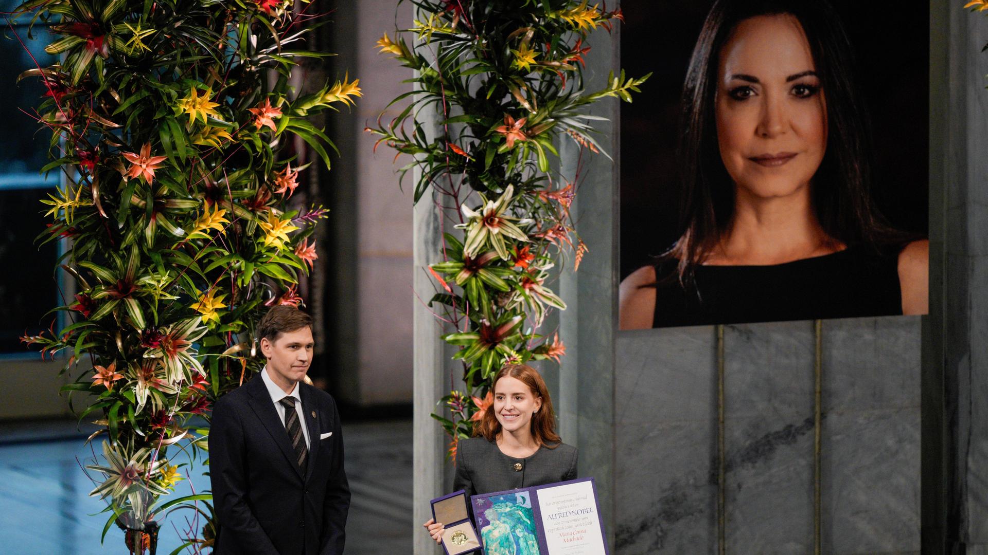 Die Tochter der Friedensnobelpreisträgerin María Corina Machado, Ana Corina Sosa, nimmt den Preis im Namen ihrer Mutter während der Verleihung im Rathaus von Oslo, Norwegen, entgegen. Im Hintergrund ist ein Foto ihrer Mutter zu sehen. Die Tochter der Friedensnobelpreisträgerin María Corina Machado, Ana Corina Sosa, nimmt den Preis im Namen ihrer Mutter während der Verleihung im Rathaus von Oslo, Norwegen, entgegen. Im Hintergrund ist ein Foto ihrer Mutter zu sehen.