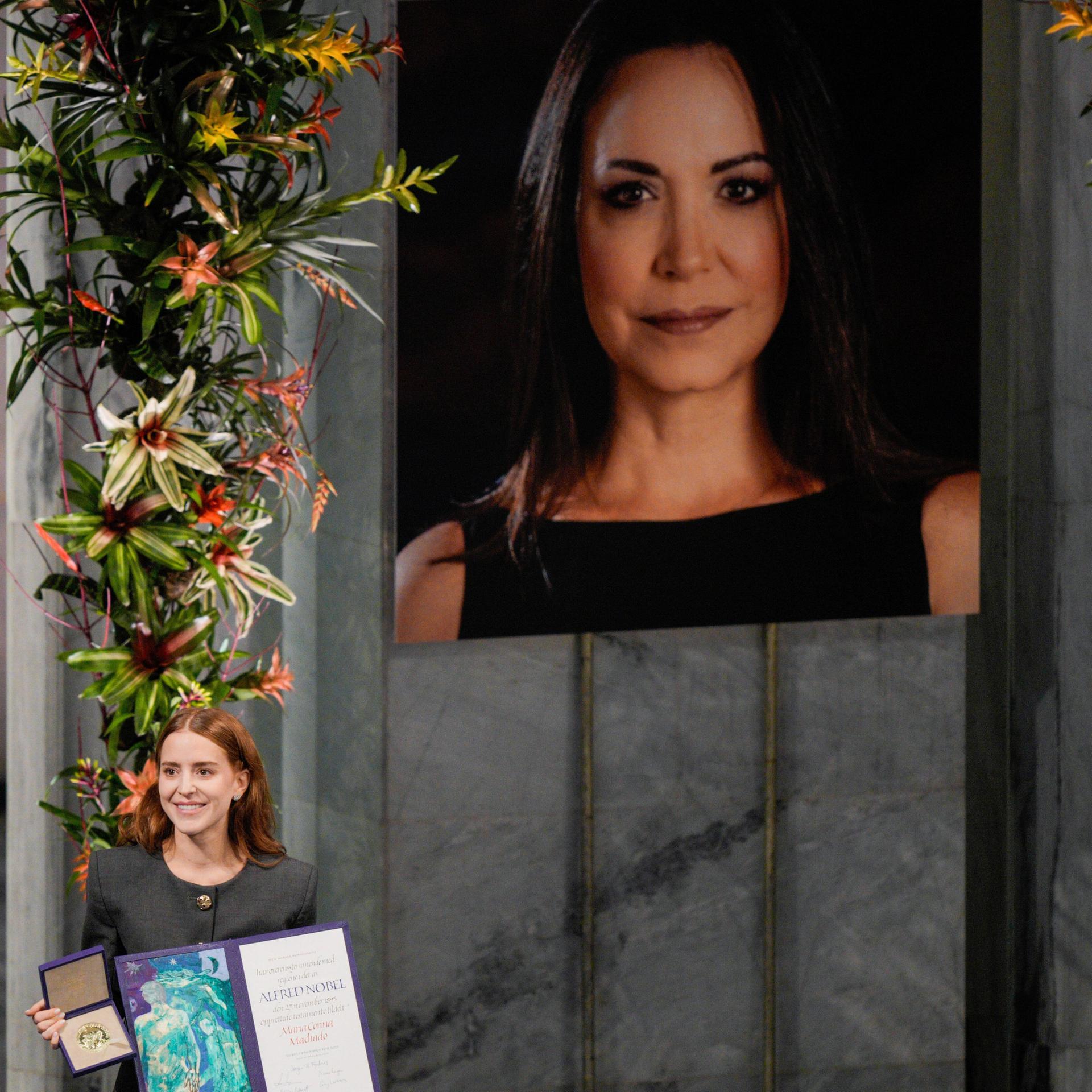 Die Tochter der Friedensnobelpreisträgerin María Corina Machado, Ana Corina Sosa, nimmt den Preis im Namen ihrer Mutter während der Verleihung im Rathaus von Oslo, Norwegen, entgegen. Im Hintergrund ist ein Foto ihrer Mutter zu sehen.