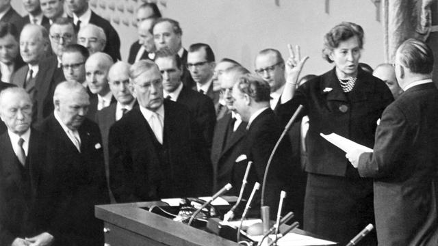 Das Schwarzweißfoto zeigt Elisabeth Schwarzhaupt am 14.11.1961 wie sie durch den Bundestagspräsidenten Eugen Gerstenmaier (r) als Bundesministerin vereidigt wird. Daneben stehen Männer. Das Schwarzweißfoto zeigt Elisabeth Schwarzhaupt am 14.11.1961 wie sie durch den Bundestagspräsidenten Eugen Gerstenmaier (r) als Bundesministerin vereidigt wird. Daneben stehen Männer.