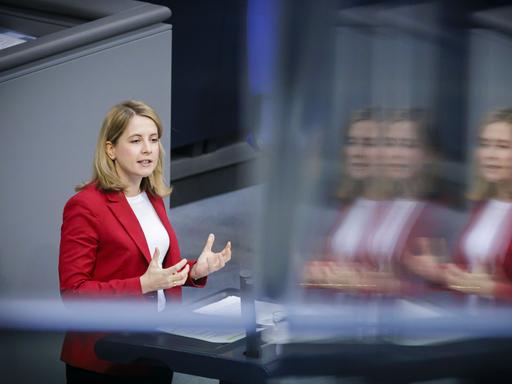 Verena Hubertz steht im Bundestag auf dem Podium und spricht. Sie hat schulterlanges bondes Haar und trägt einen roten Blazer.