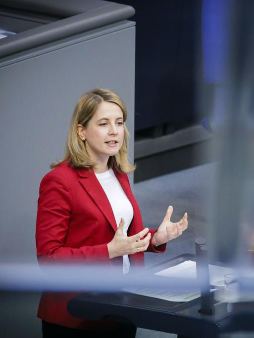 Verena Hubertz steht im Bundestag auf dem Podium und spricht. Sie hat schulterlanges bondes Haar und trägt einen roten Blazer.