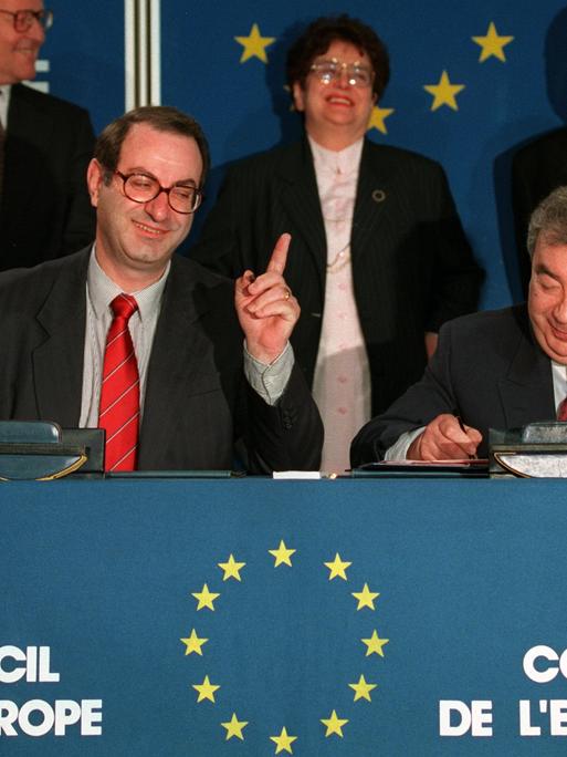 Der Generalsekretär des Europarats, Daniel Tarschys (links im Bild) gestikuliert, während der russische Außenminister, Jewgeni Primakow, am 28. Februar 1996 in Straßburg das Dokument über die Aufnahme Russlands unterzeichnet.