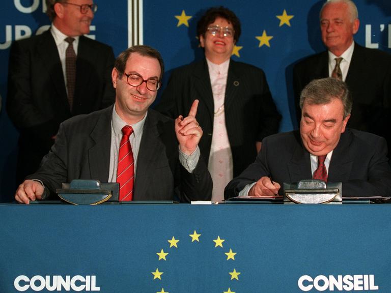 Der Generalsekretär des Europarats, Daniel Tarschys (links im Bild) gestikuliert, während der russische Außenminister, Jewgeni Primakow, am 28. Februar 1996 in Straßburg das Dokument über die Aufnahme Russlands unterzeichnet.