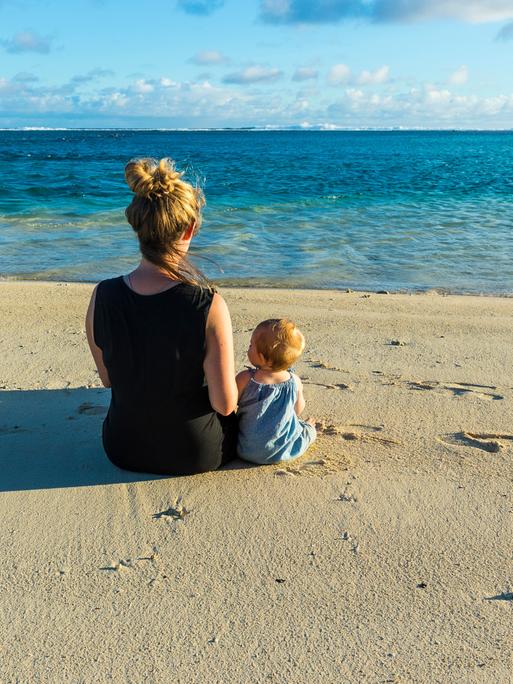 Eine Frau und ein Kind sitzen am Strand und schauen auf das Meer